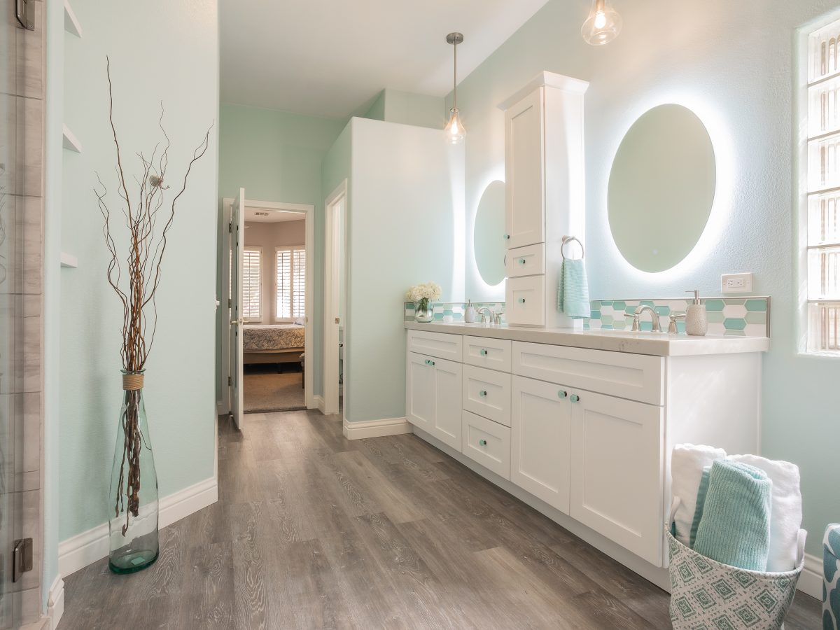 Coastal primary bathroom with backlit round mirrors, white quartz vanity, and teal hex mosaic tile, Reveal Interior Design Las Vegas