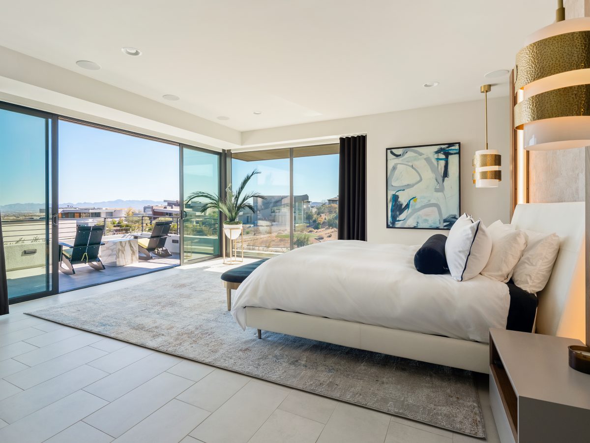 Primary bedroom with floor-to-ceiling walnut headboard wall and panoramic Las Vegas skyline views, Reveal Interior Design Las Vegas