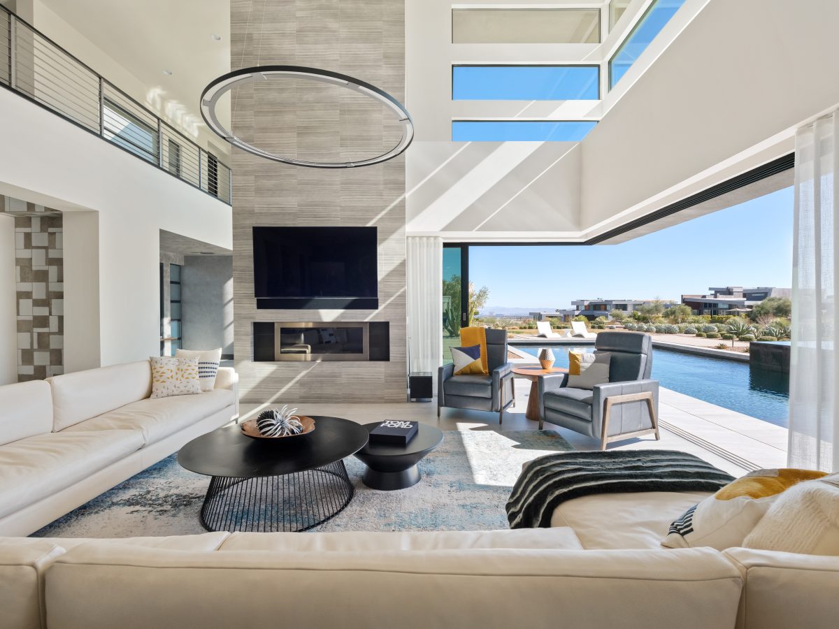 Double-height living room with custom sectional, ring LED pendant, and open-slider indoor-outdoor flow, Reveal Interior Design Las Vegas