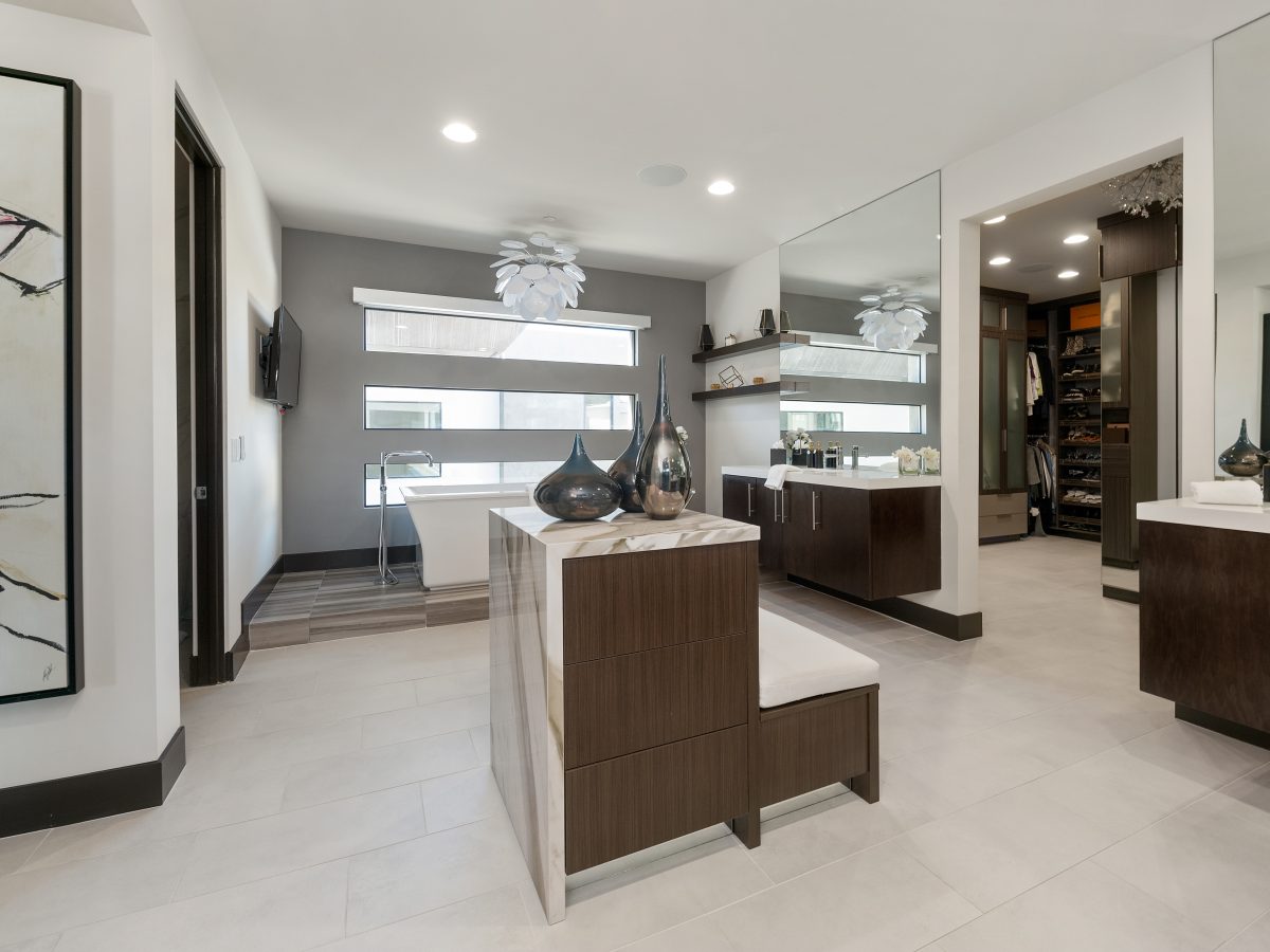 Primary bathroom with floating dark-stained vanities, custom storage island, and marble-look porcelain slab, Reveal Interior Design Las Vegas