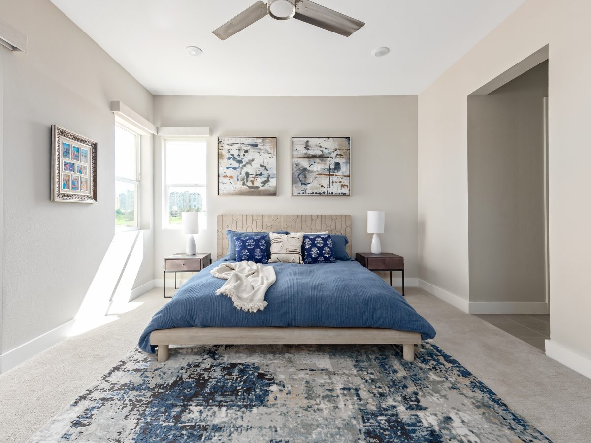 Primary bedroom with carved warm wood headboard, blue duvet bedding, and stainless ceiling fan, Reveal Interior Design Las Vegas