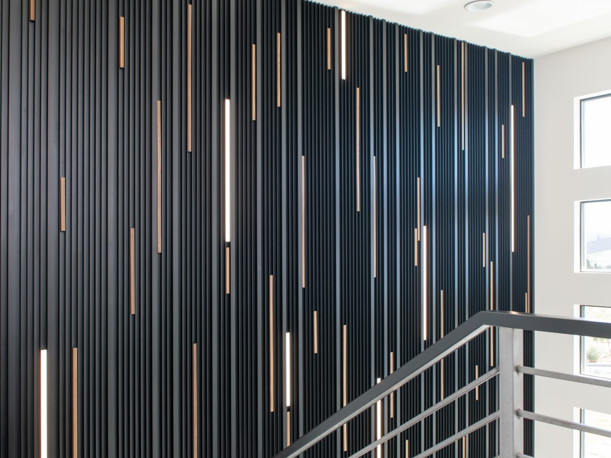 Entryway stairwell with extruded black metal dimensional panels, LED lighting, and walnut strip accents, Reveal Interior Design Las Vegas