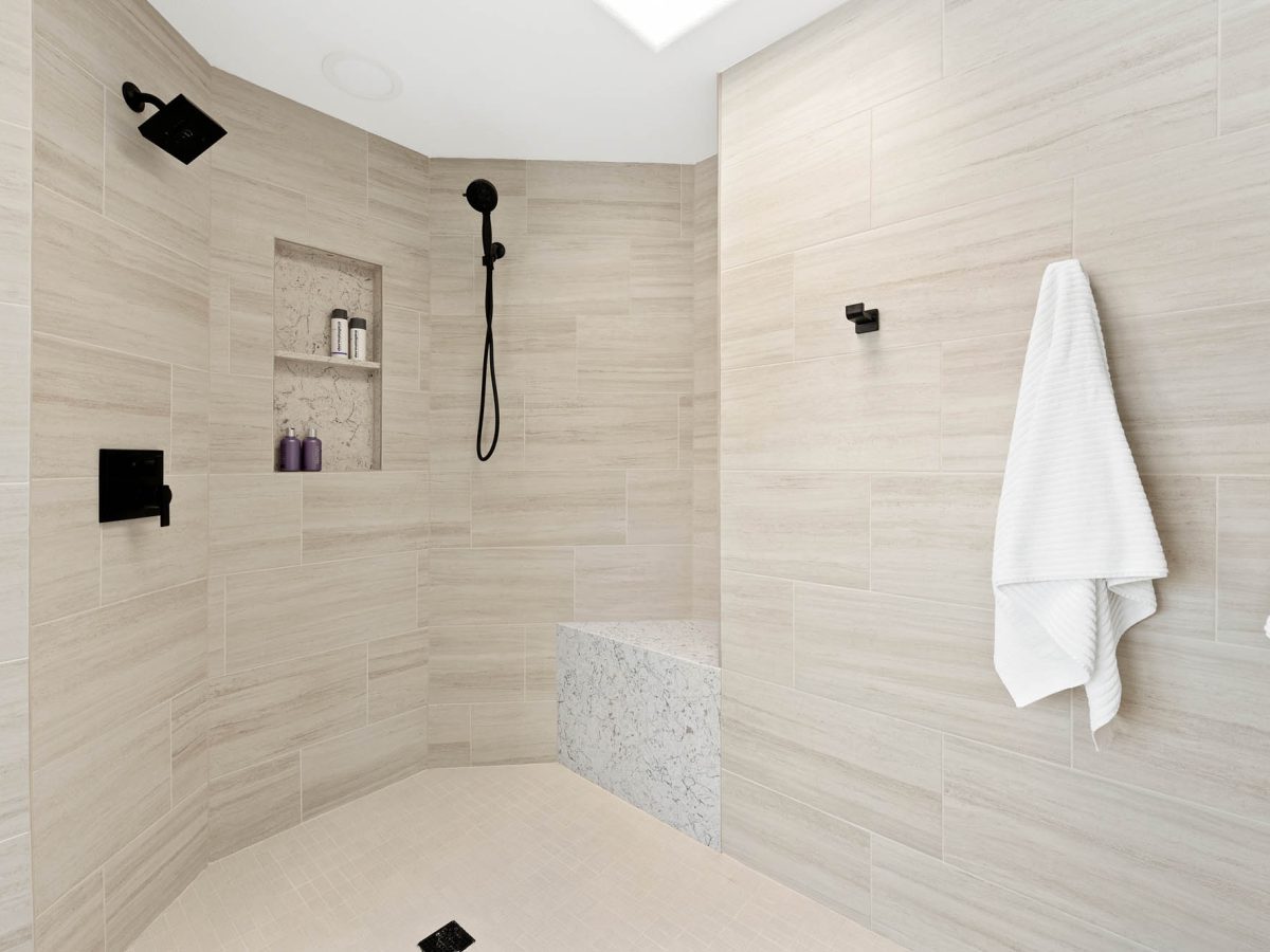 Primary bathroom angled walk-in shower with built-in bench, dual-level niche, and matte black fixtures, Reveal Interior Design Las Vegas
