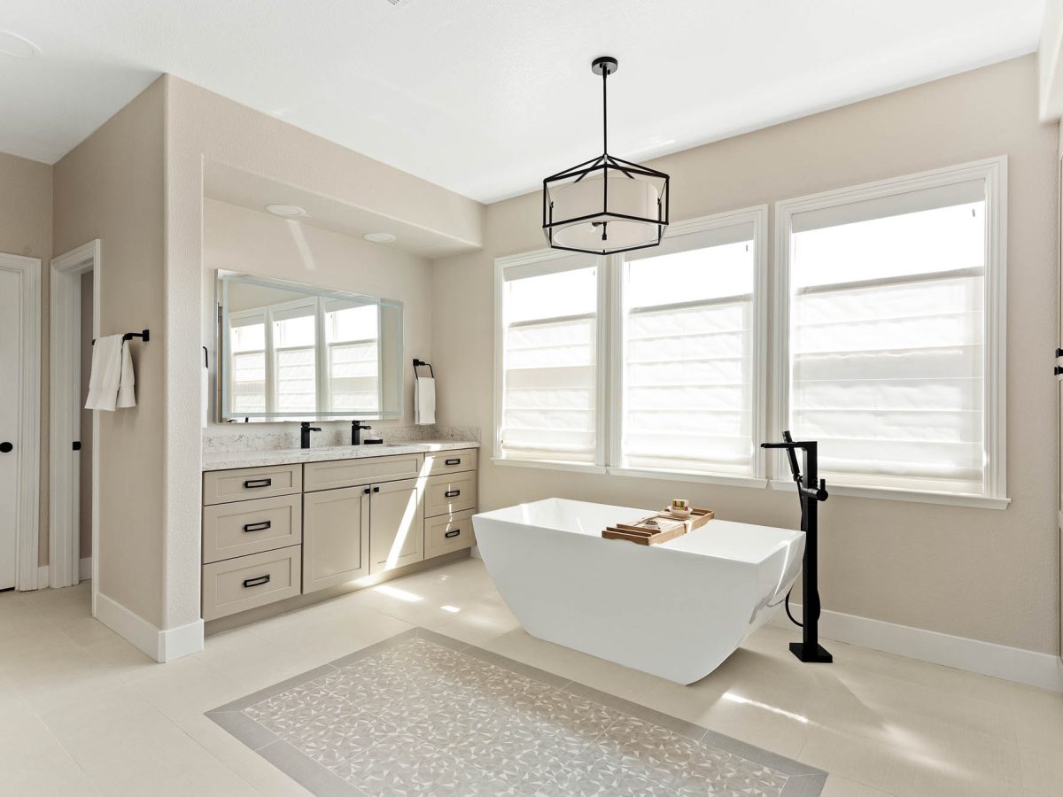 Primary bathroom with freestanding soaking tub, warm beige cabinetry, and quartz countertops, Reveal Interior Design Las Vegas