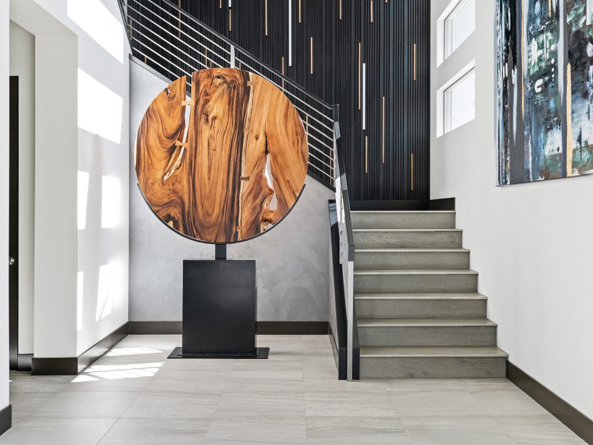 Dramatic entryway with large round wood sculpture, dimensional black metal stairwell wall, and LED-lit walnut strips, Reveal Interior Design Las Vegas