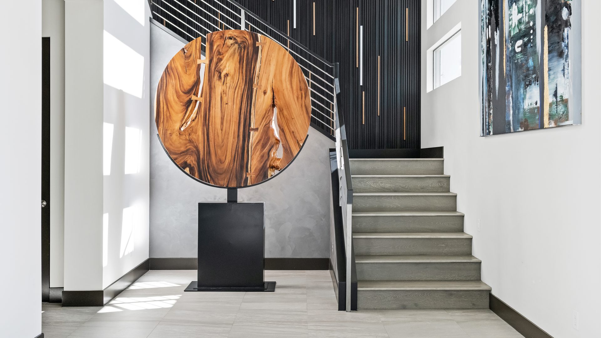Dramatic entryway with large round wood sculpture, dimensional black metal stairwell wall, and LED-lit walnut strips, Reveal Interior Design Las Vegas