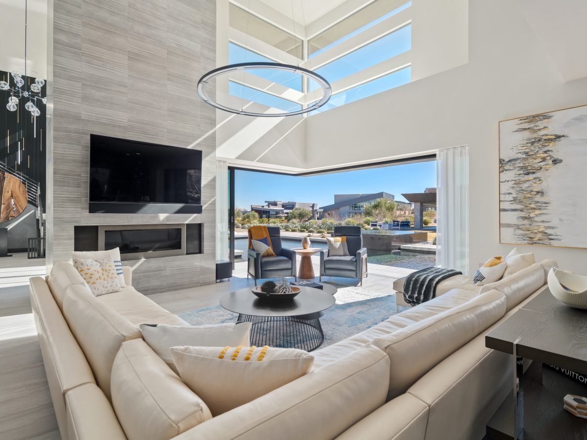 Double-height living room with custom sectional, ring LED pendant, and open glass slider, Reveal Interior Design Las Vegas