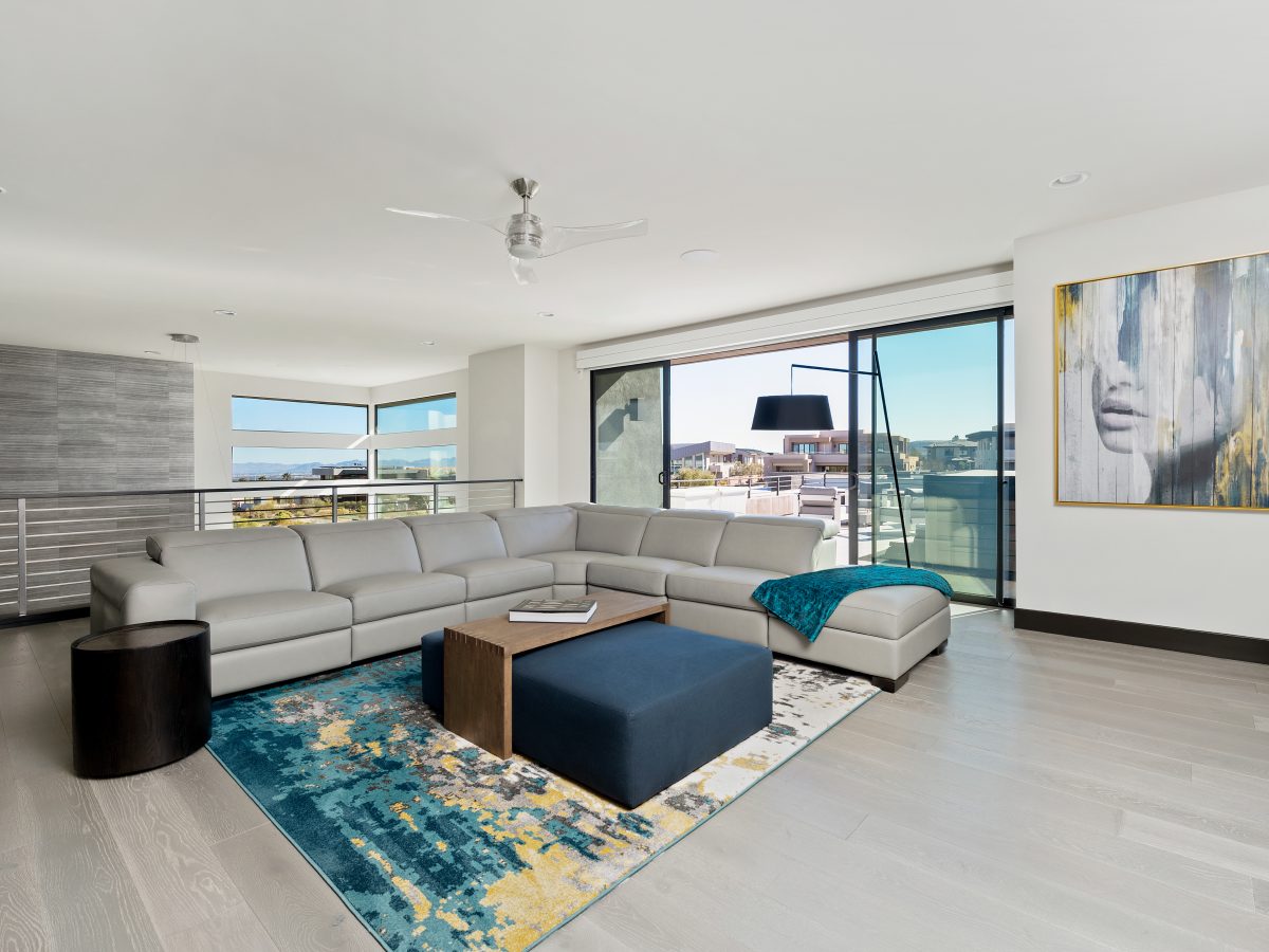 Upstairs loft seating area with leather motion sectional, bold teal-and-yellow rug, and open patio views, Reveal Interior Design Las Vegas