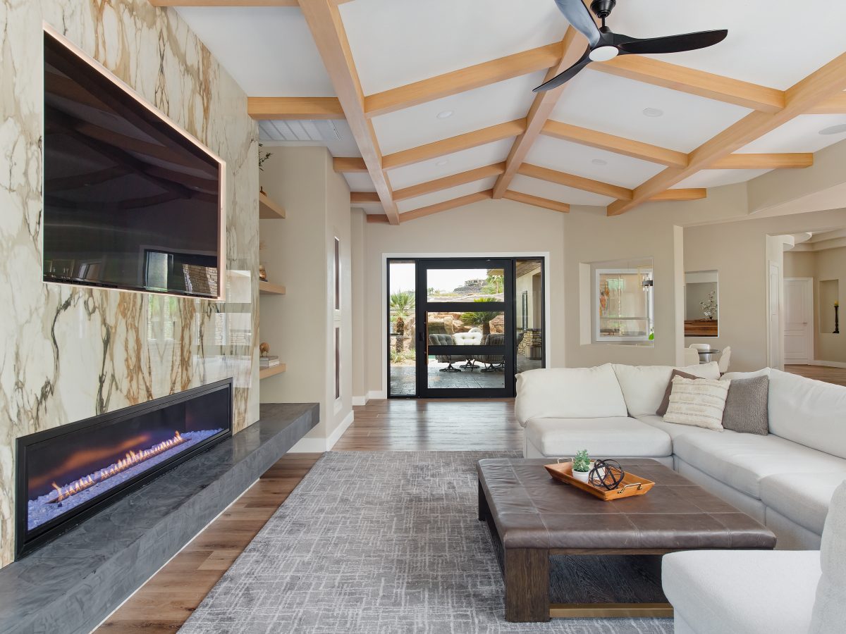 Living room with bookmatched porcelain fireplace surround, backlit TV, and oak beam ceiling, Reveal Interior Design Las Vegas