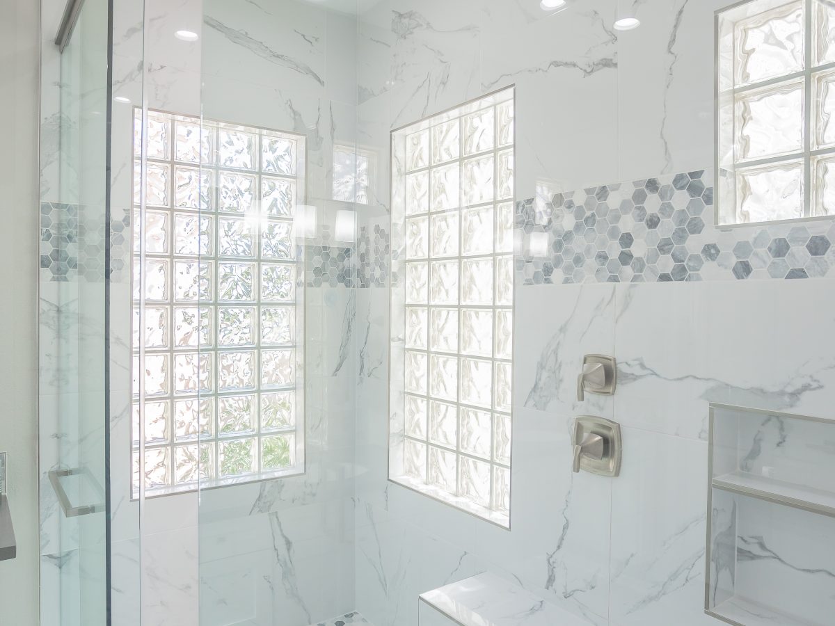 Primary bathroom with marble-look porcelain shower walls, geometric mosaic tile accents, and ceiling-mount rain showerhead, Reveal Interior Design Las Vegas