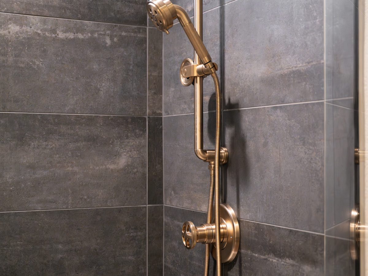Luxury shower with brushed brass slide bar, handheld fixture, and dark stone tile, Reveal Interior Design Las Vegas