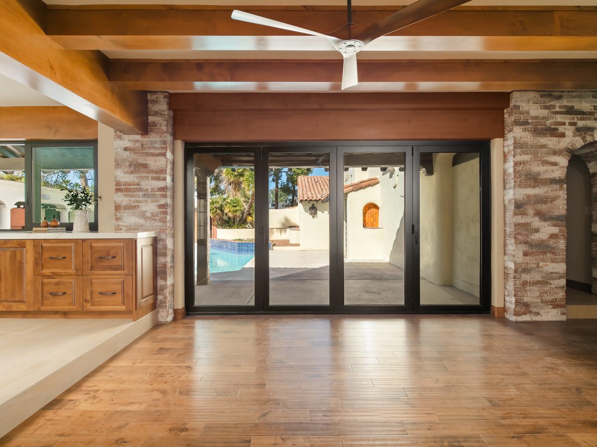 Open living room with travertine-style fireplace, engineered wood flooring, and bronze multi-panel patio doors, Reveal Interior Design Las Vegas