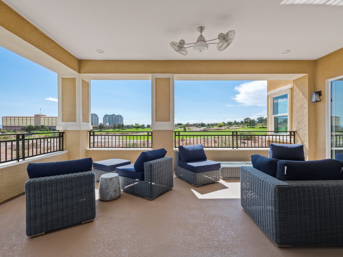 Covered outdoor patio with gray rattan seating, navy cushions, and rotating ceiling fan, Reveal Interior Design Las Vegas