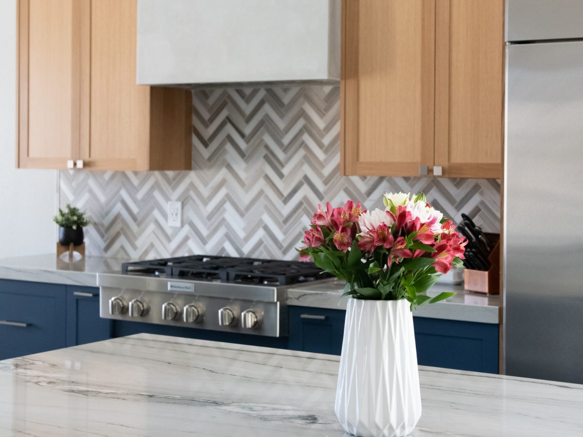 Kitchen with dark blue base cabinets, warm oak uppers, quartzite island countertop, and herringbone mosaic backsplash, Reveal Interior Design Las Vegas