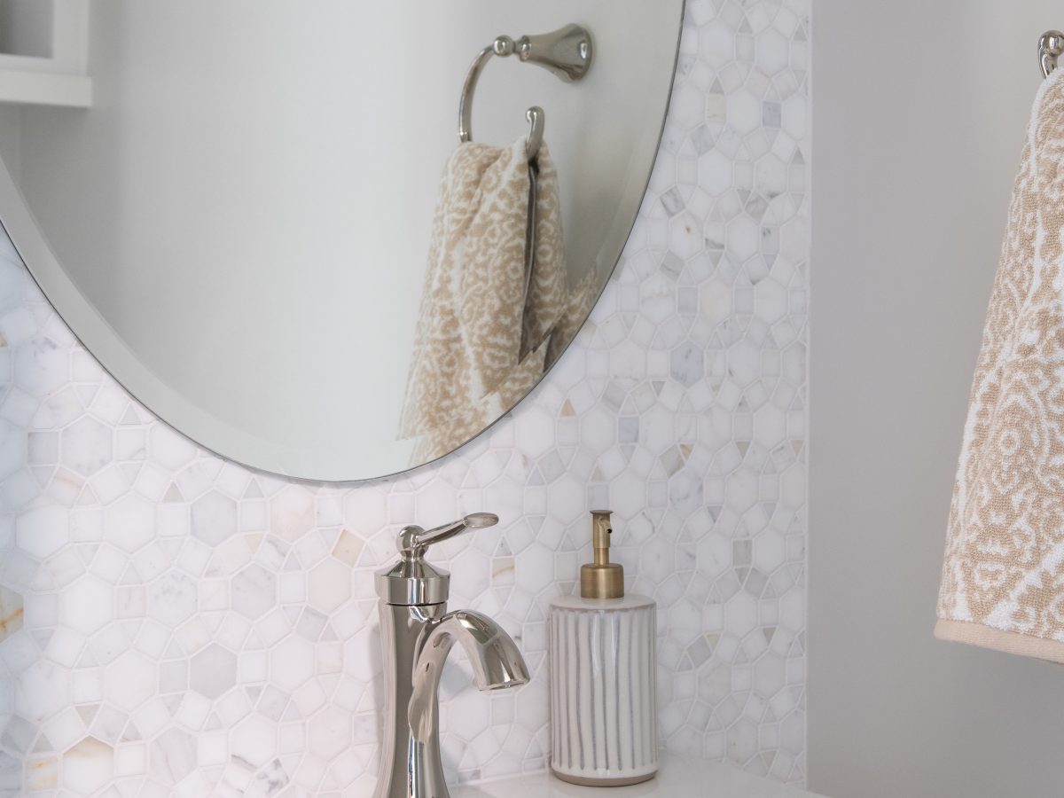 Powder bath with geometric marble mosaic tile wall, oval mirror, and polished nickel faucet, Reveal Interior Design Las Vegas