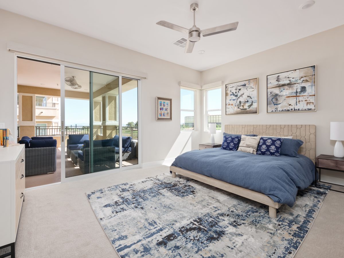 Coastal primary bedroom with blue duvet, carved wood headboard, and balcony access, Reveal Interior Design Las Vegas