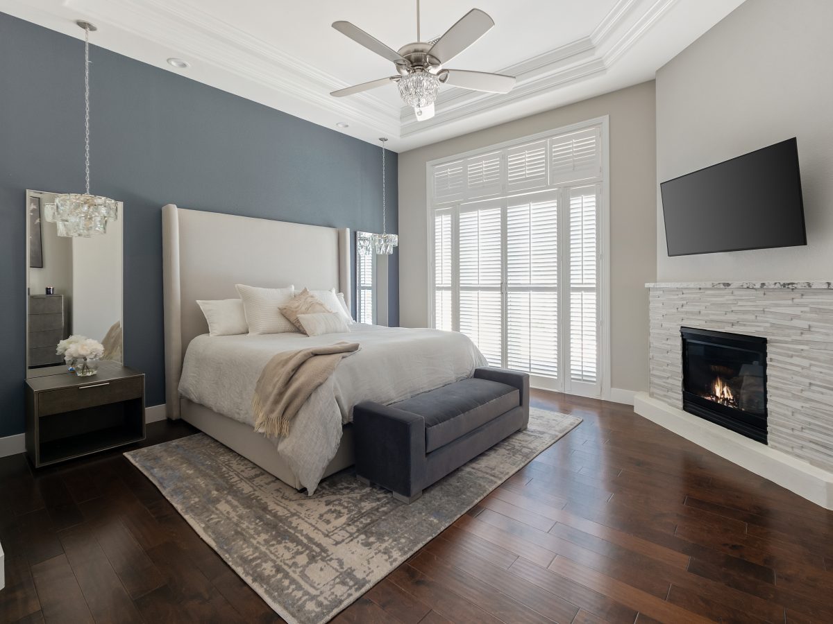 Primary bedroom with slate blue accent wall, cherry engineered wood floors, and stone fireplace, Reveal Interior Design Las Vegas