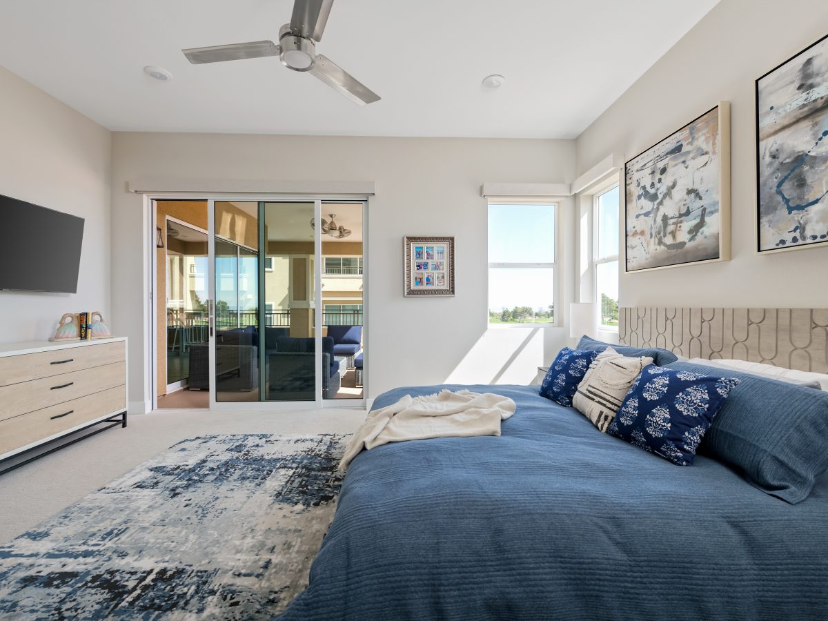 Primary bedroom with carved natural wood headboard, blue duvet bedding, and stainless ceiling fan, Reveal Interior Design Las Vegas