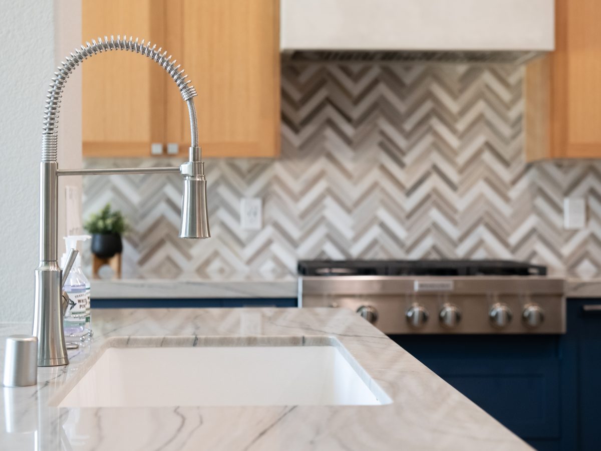 Kitchen with quartzite island countertop, brushed nickel spring faucet, and stone herringbone mosaic backsplash, Reveal Interior Design Las Vegas