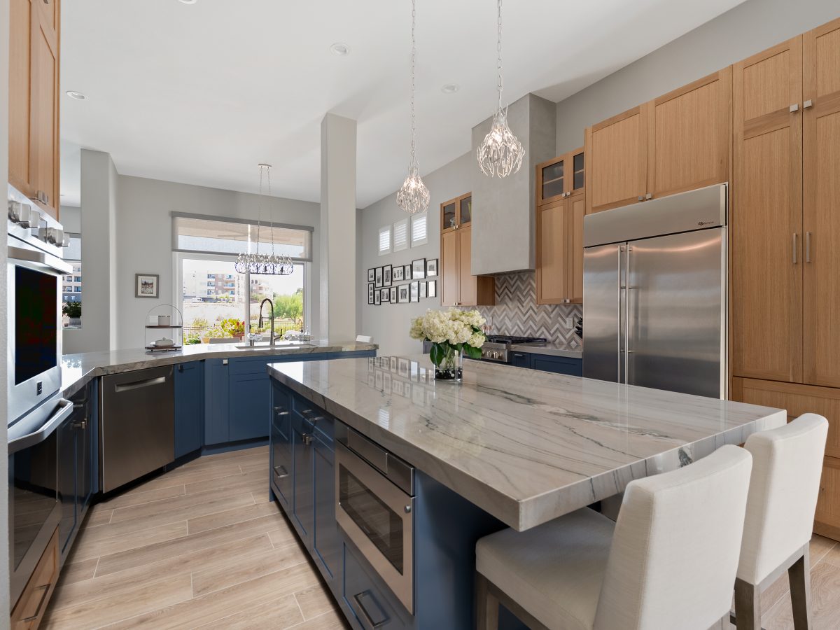 Kitchen with quartzite island, dark blue and warm oak cabinetry, stone herringbone backsplash, Reveal Interior Design Las Vegas