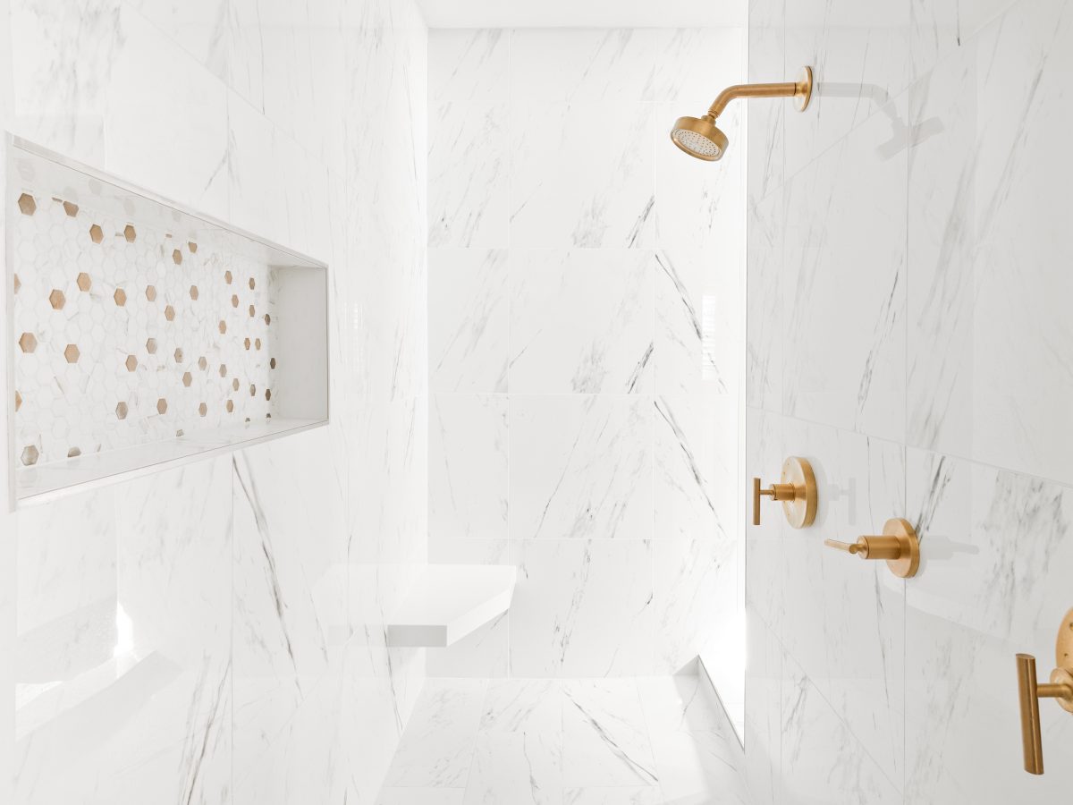 Primary bathroom shower with Calacatta-look porcelain tile walls and brushed gold fixtures, Reveal Interior Design Las Vegas