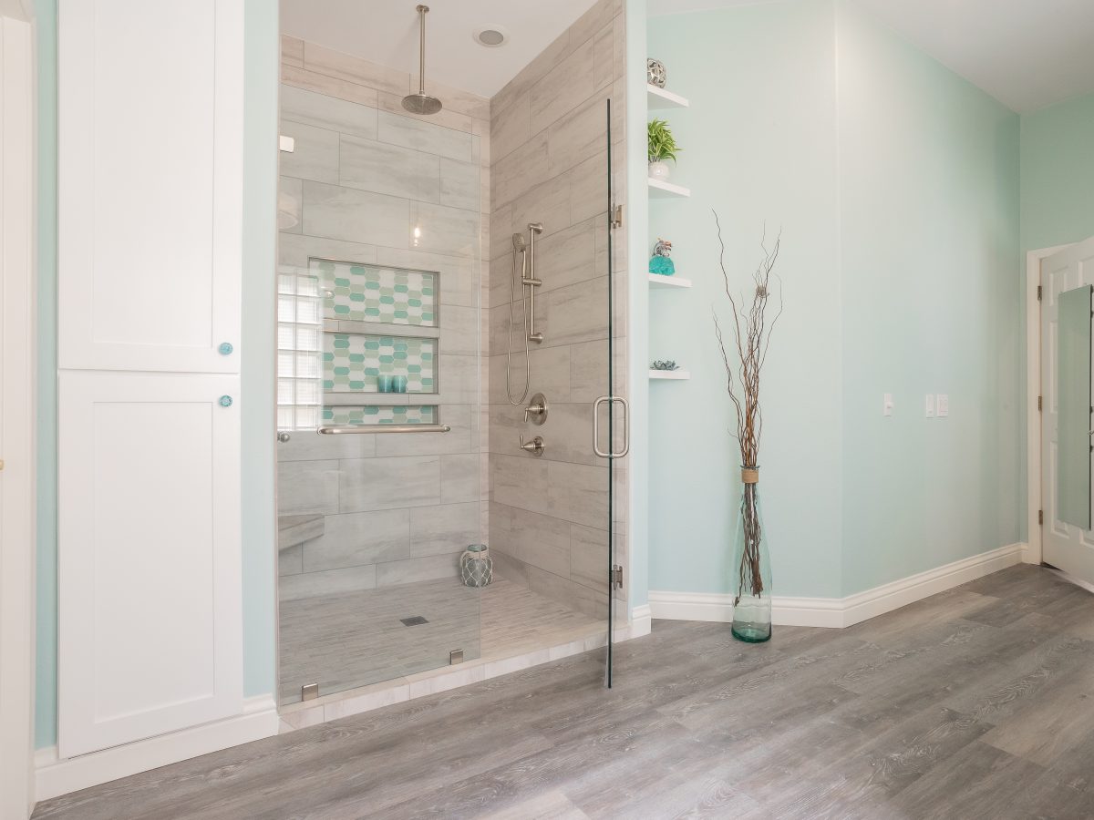 Beach-inspired primary bathroom with frameless glass shower, stone-look porcelain tile, and wood-look plank flooring, Reveal Interior Design Las Vegas