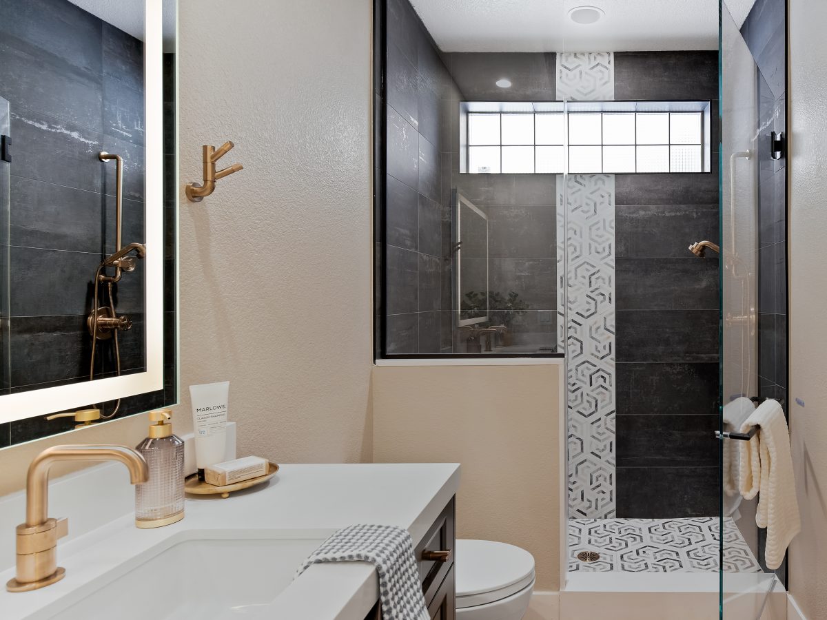 Contemporary guest bathroom with dark tile shower, geometric mosaic floor, and brushed gold fixtures, Reveal Interior Design Las Vegas