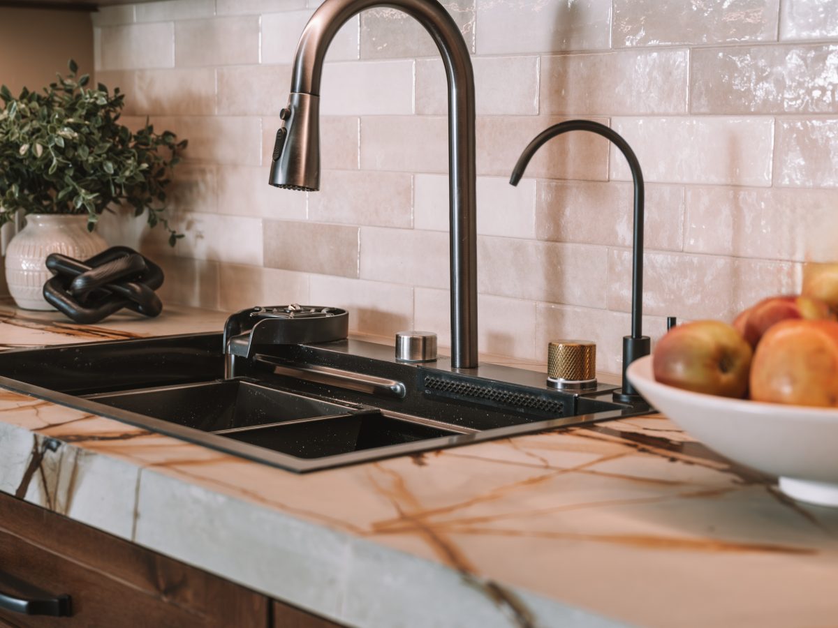 Kitchen sink area with stone-detailed apron front sink, oil rubbed bronze faucets, and marbled-look quartz countertops, Reveal Interior Design Las Vegas