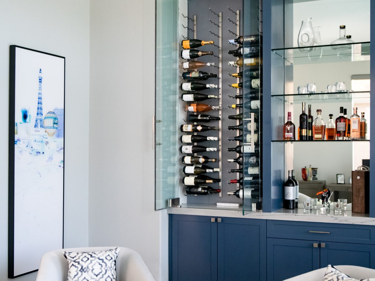 Lounge bar with blue cabinetry, glass-enclosed dual-zone wine storage and mirrored shelving, Reveal Interior Design Las Vegas
