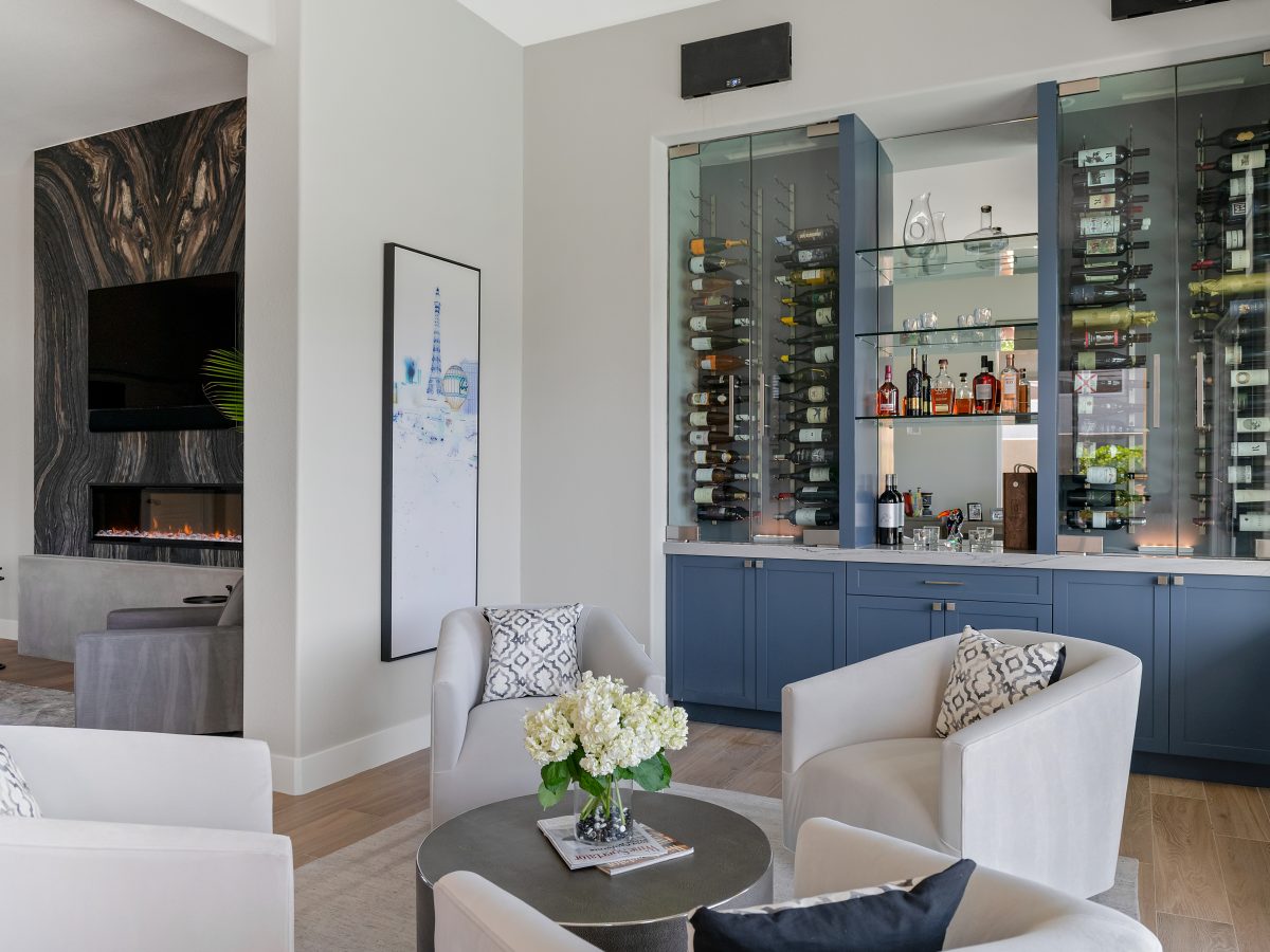 Lounge bar with blue cabinetry, glass-enclosed dual-zone wine coolers, and swivel seating, Reveal Interior Design Las Vegas