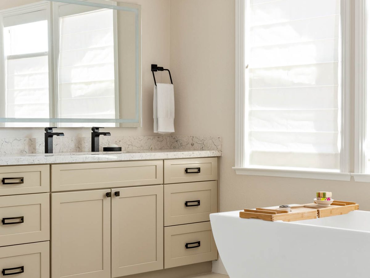 Primary bathroom with warm beige cabinetry, quartz countertops, and freestanding tub, Reveal Interior Design Las Vegas