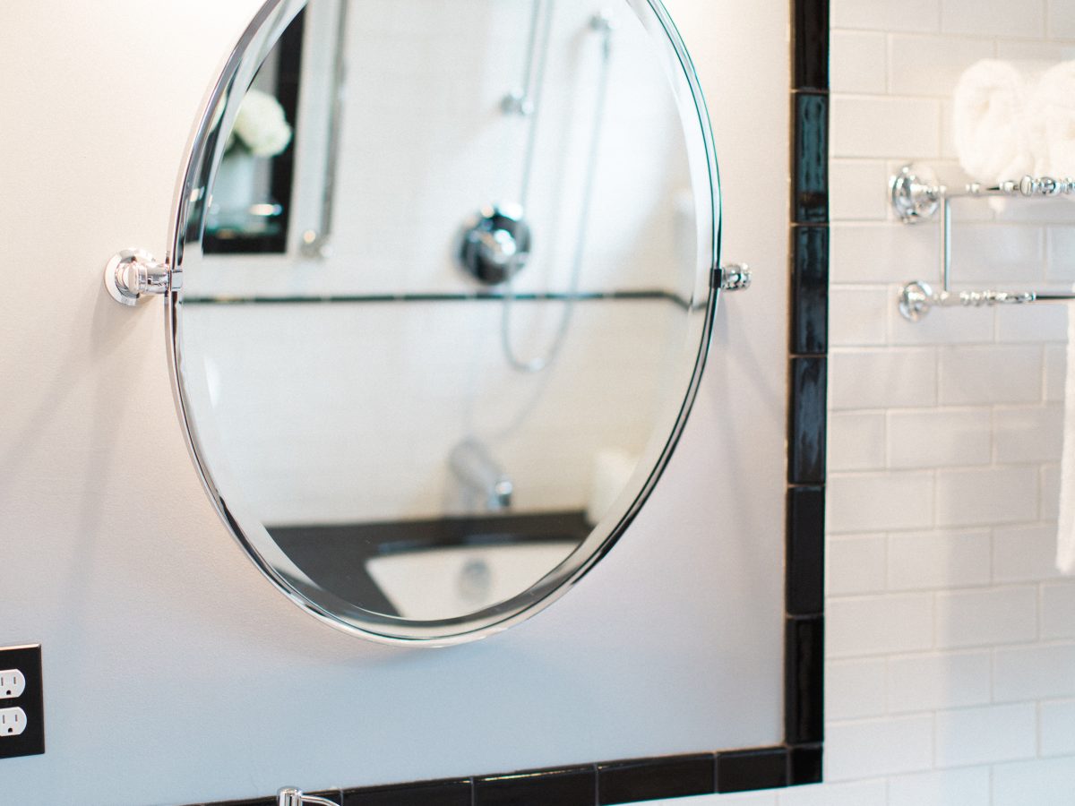 Classic black-and-white bathroom with oval tilt mirror, chrome fixtures, and subway tile wainscoting, Reveal Interior Design Las Vegas