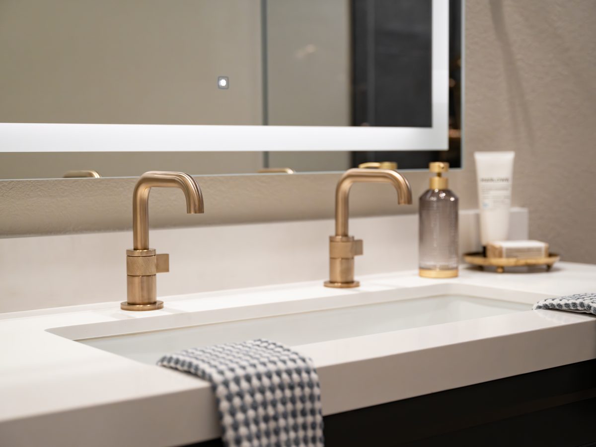Luxury double-faucet bathroom sink with brushed brass fixtures and integrated white basin, Reveal Interior Design Las Vegas