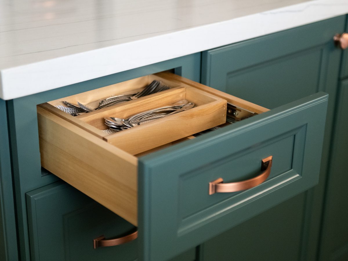 Kitchen drawer with wood cutlery organizer, emerald cabinetry, and copper hardware, Reveal Interior Design Las Vegas
