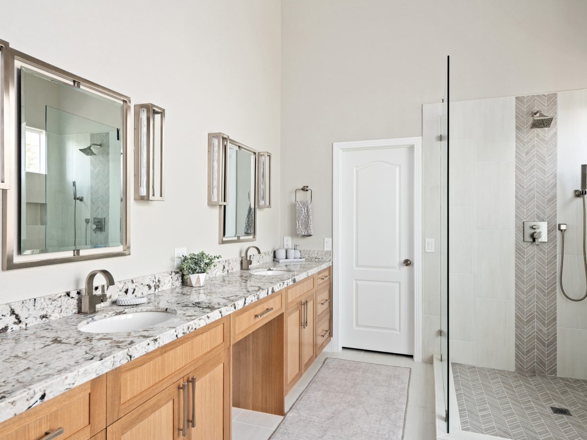Primary bathroom with warm oak vanity, granite countertops, and glass-enclosed shower, Reveal Interior Design Las Vegas