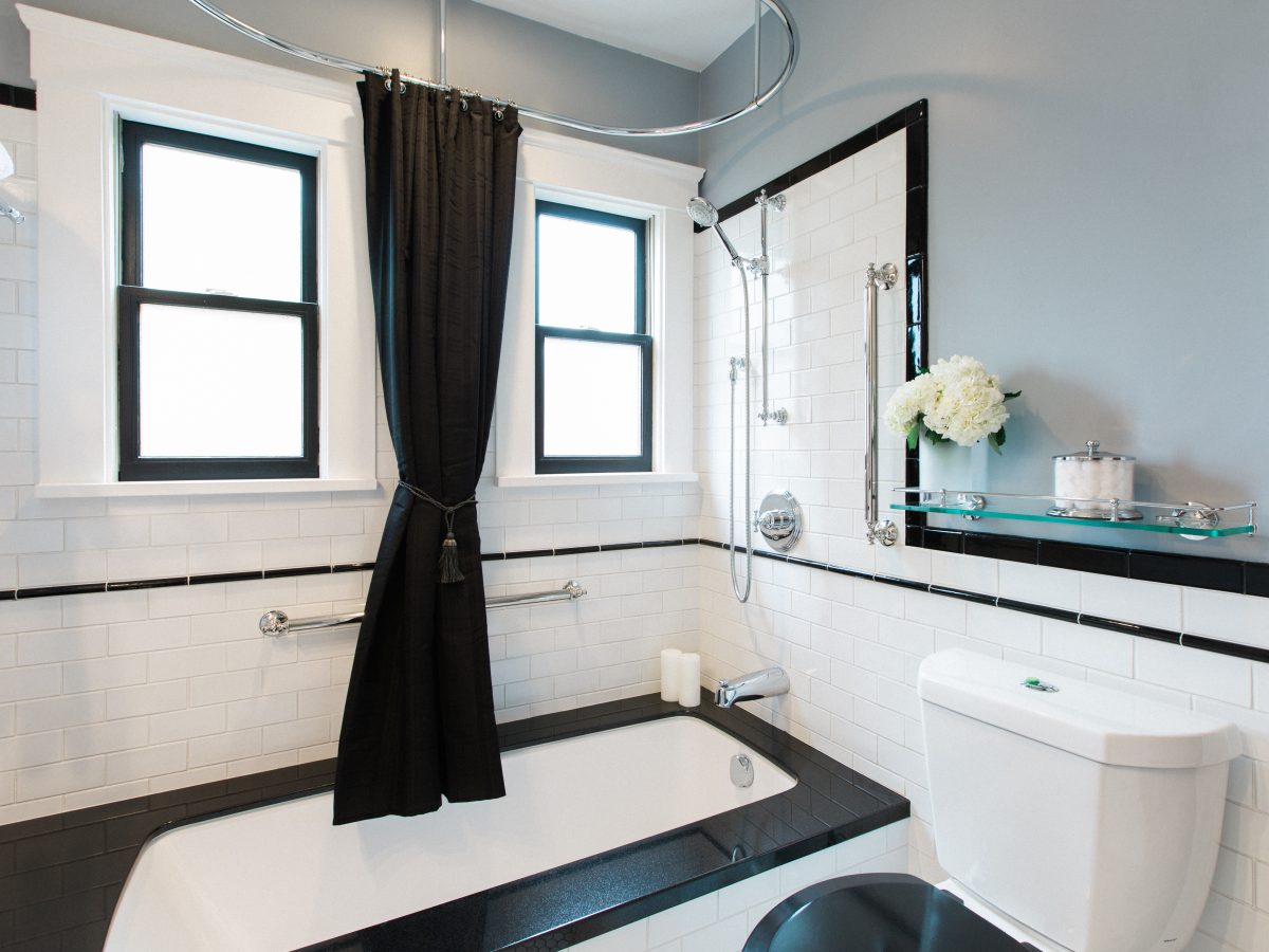 1920s-style black and white bathroom with black granite tub surround and subway tile wainscoting, Reveal Interior Design Las Vegas