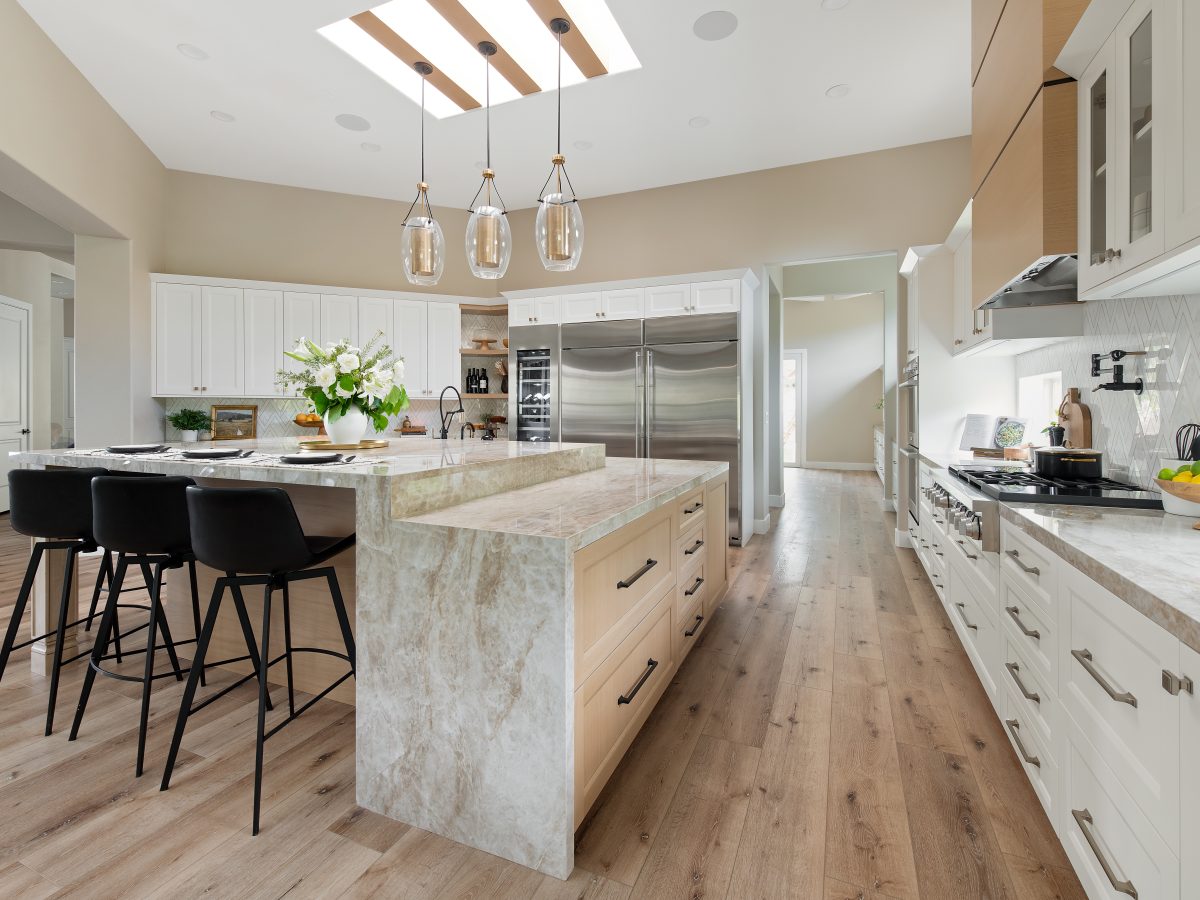 Luxury kitchen with Dekton Taj Mahal island, brushed brass accents, and skylight beams, Reveal Interior Design Las Vegas
