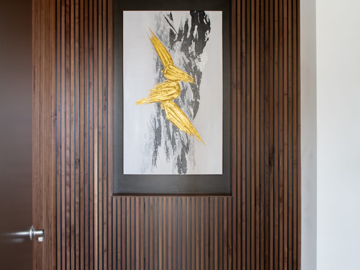 Wood slat entry wall with recessed art niche and gold bird artwork, Reveal Interior Design Las Vegas